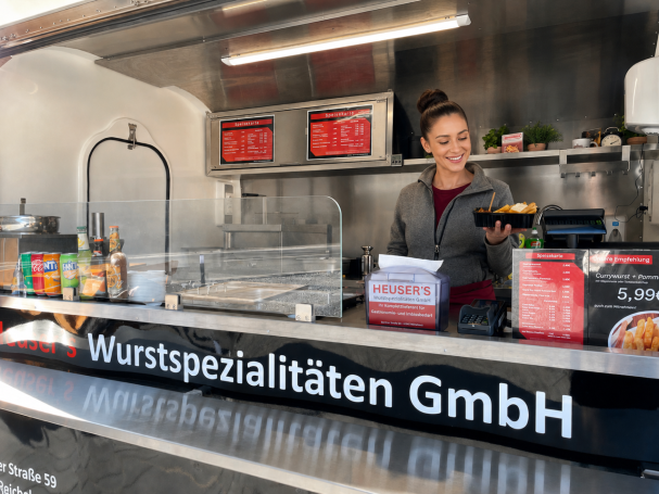 Frau an einem Foodtruck, der Wurstwaren und Snacks anbietet.